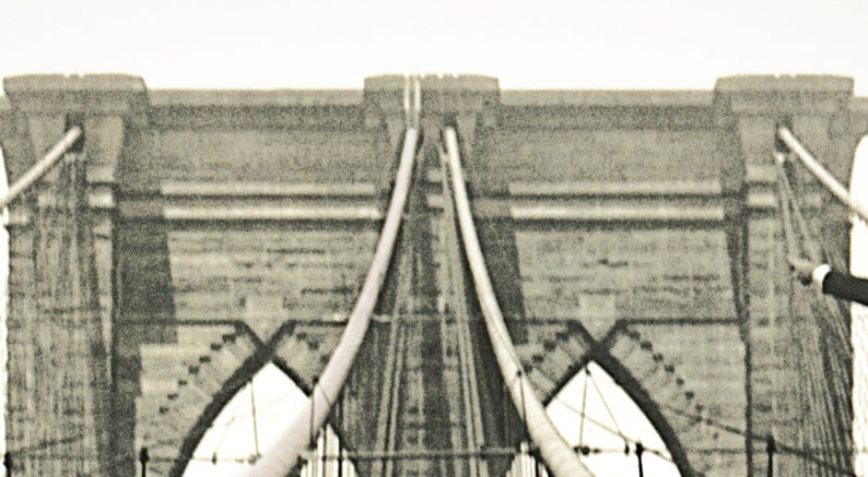 Puede incluir: Imagen en tonos sepia del puente de Brooklyn, mostrando su ic&oacute;nica arquitectura. Las torres de piedra y los cables de suspensi&oacute;n del puente son prominentes, con un cielo despejado en el fondo. La imagen captura el dise&ntilde;o sim&eacute;trico del puente.