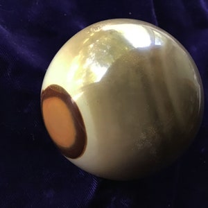 May include: A smooth, round, light brown sphere with a dark brown ring and a smaller orange circle inside the ring.