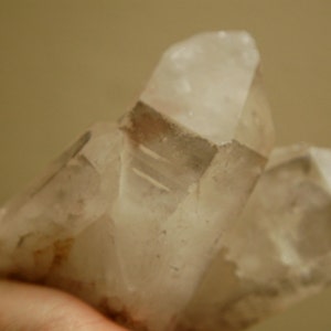 Puede incluir: Un grupo de cristales de cuarzo transparente con una apariencia ligeramente turbia. Los cristales tienen puntas geométricas afiladas y exhiben sutiles inclusiones marrones. La forma general es irregular, con múltiples formaciones cristalinas.