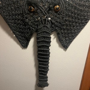 May include: A black macrame elephant wall hanging with two round, yellow and black eyes.