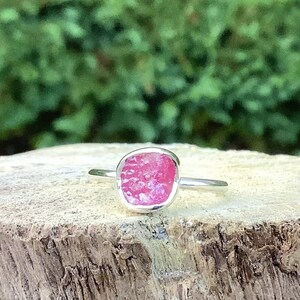 May include: A silver ring featuring a pink, rough-cut gemstone set in a bezel setting.