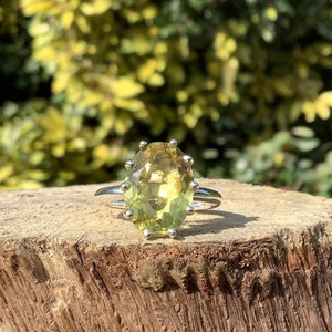 May include: A silver ring featuring a large, oval-shaped, light green gemstone. The gemstone is set in a prong setting with small silver accents.