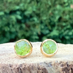 May include: A pair of gold earrings with green gemstone accents. The earrings are small and round, and the gemstones are set in a bezel setting.