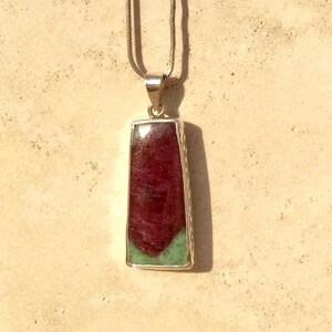 May include: A silver chain necklace with a rectangular pendant featuring a green and red gemstone.