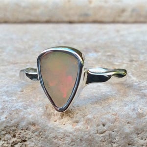 Peut inclure: Une bague en argent avec une pierre pr&eacute;cieuse en opale triangulaire. L'opale est d'un blanc p&acirc;le avec des nuances de rose et de vert.