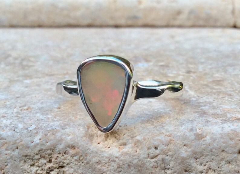 Peut inclure: Une bague en argent avec une pierre pr&eacute;cieuse en opale triangulaire. L'opale est d'un blanc p&acirc;le avec des nuances de rose et de vert.