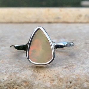 Peut inclure: Une bague en argent avec une pierre pr&eacute;cieuse en opale de forme larme. L'opale est de couleur blanc laiteux avec des nuances de rose et de jaune.