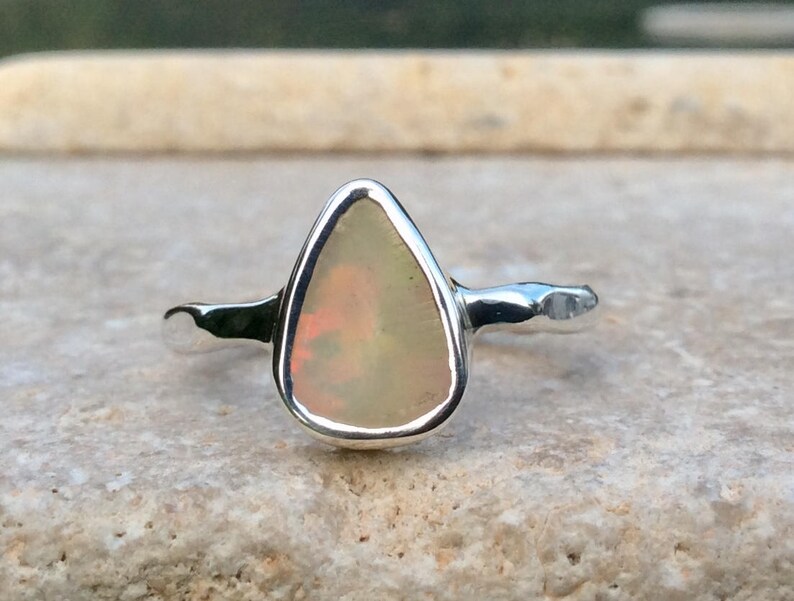 Peut inclure: Une bague en argent avec une pierre pr&eacute;cieuse en opale de forme larme. L'opale est de couleur blanc laiteux avec des nuances de rose et de jaune.