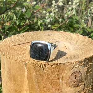 May include: A silver ring with a square black gemstone. The ring is sitting on a wooden surface.