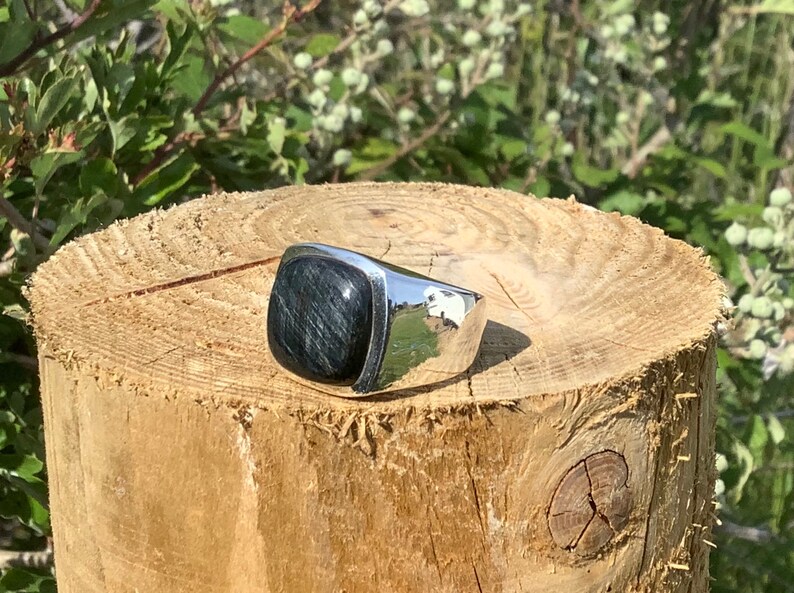 May include: A silver ring with a square-shaped black gemstone. The ring is sitting on a wooden surface.