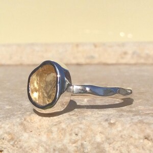 Puede incluir: Un anillo de plata con una piedra preciosa amarilla engastada en un engaste texturizado. La banda est&aacute; martillada y tiene un dise&ntilde;o ondulado.