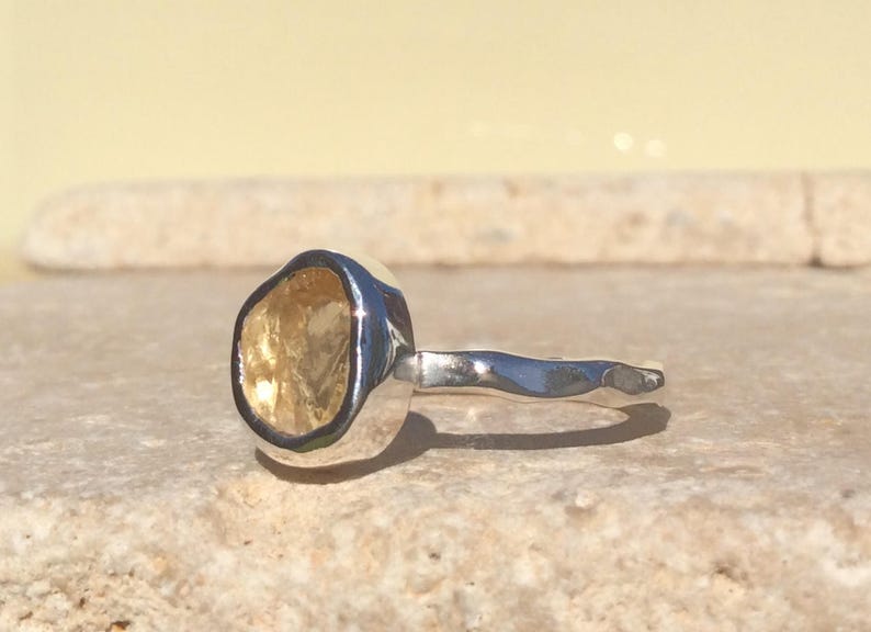 Puede incluir: Un anillo de plata con una piedra preciosa amarilla engastada en un engaste texturizado. La banda est&aacute; martillada y tiene un dise&ntilde;o ondulado.