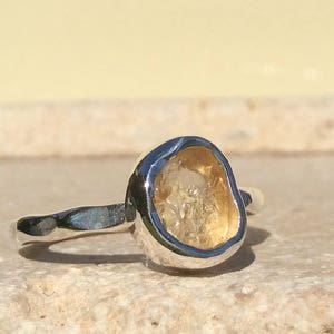 Puede incluir: Un anillo de plata con una piedra preciosa amarilla engastada en una forma irregular y &uacute;nica.