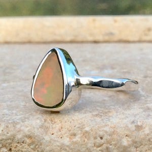 Peut inclure: Une bague en argent avec une pierre d'opale en forme de larme. L'opale est de couleur rose p&acirc;le avec un l&eacute;ger &eacute;clat iridescent.