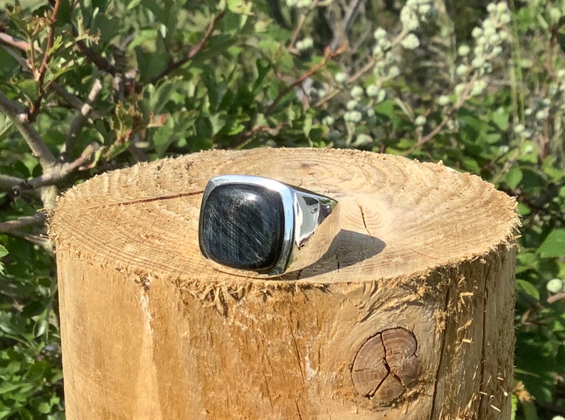 May include: A silver ring with a square-shaped blue gemstone. The ring is sitting on a wooden surface.