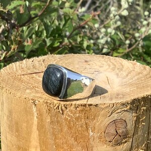 May include: A silver ring with a dark blue gemstone. The ring is set on a wooden surface.