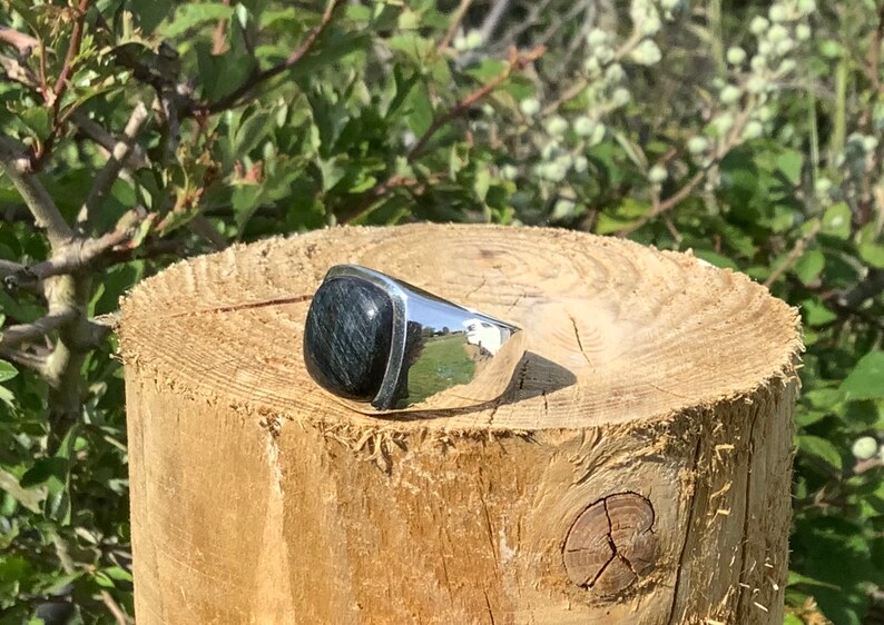 May include: A silver ring with a dark blue gemstone. The ring is set on a wooden surface.
