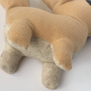 Peut inclure: Une peluche en forme de chien, principalement beige avec des accents beige clair sur les pattes et le ventre. L'&oelig;il du chien est noir et blanc. Le jouet est fait d'une mati&egrave;re douce semblable &agrave; du feutre.