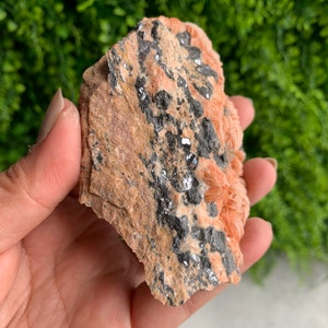 May include: A rough, orange-brown rock with black and silver crystals embedded in it.