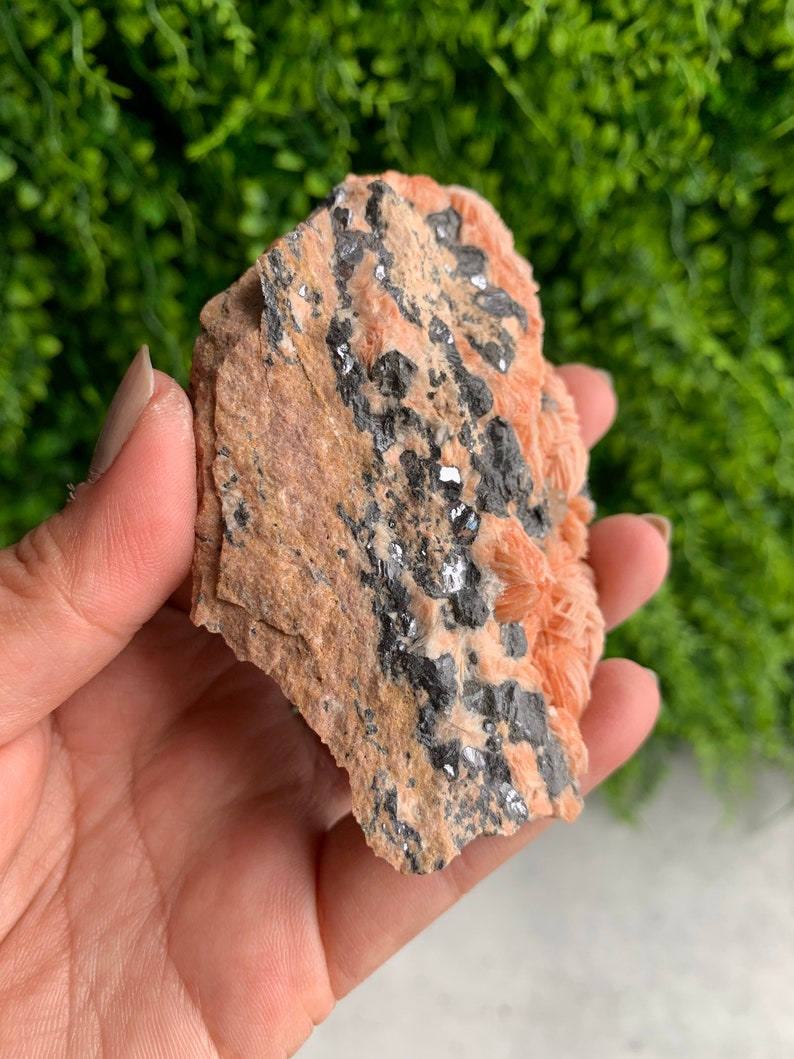 May include: A rough, orange-brown rock with black and silver crystals embedded in it.