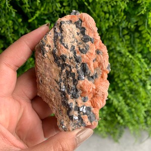 May include: A raw, pink and gray crystal cluster with a rough, natural texture. The crystal is a combination of pink and gray, with a rough, natural texture.
