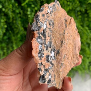 May include: A close-up of a raw, natural, orange and brown stone with black and silver crystals embedded in it.
