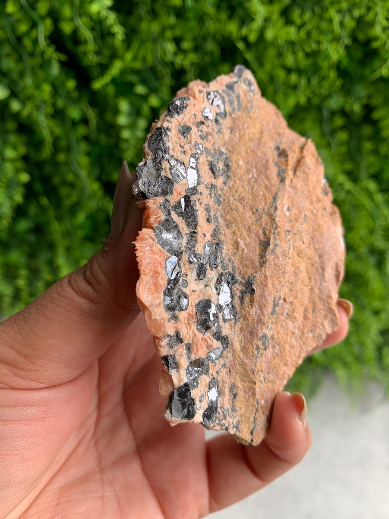 May include: A close-up of a raw, natural, orange and brown stone with black and silver crystals embedded in it.