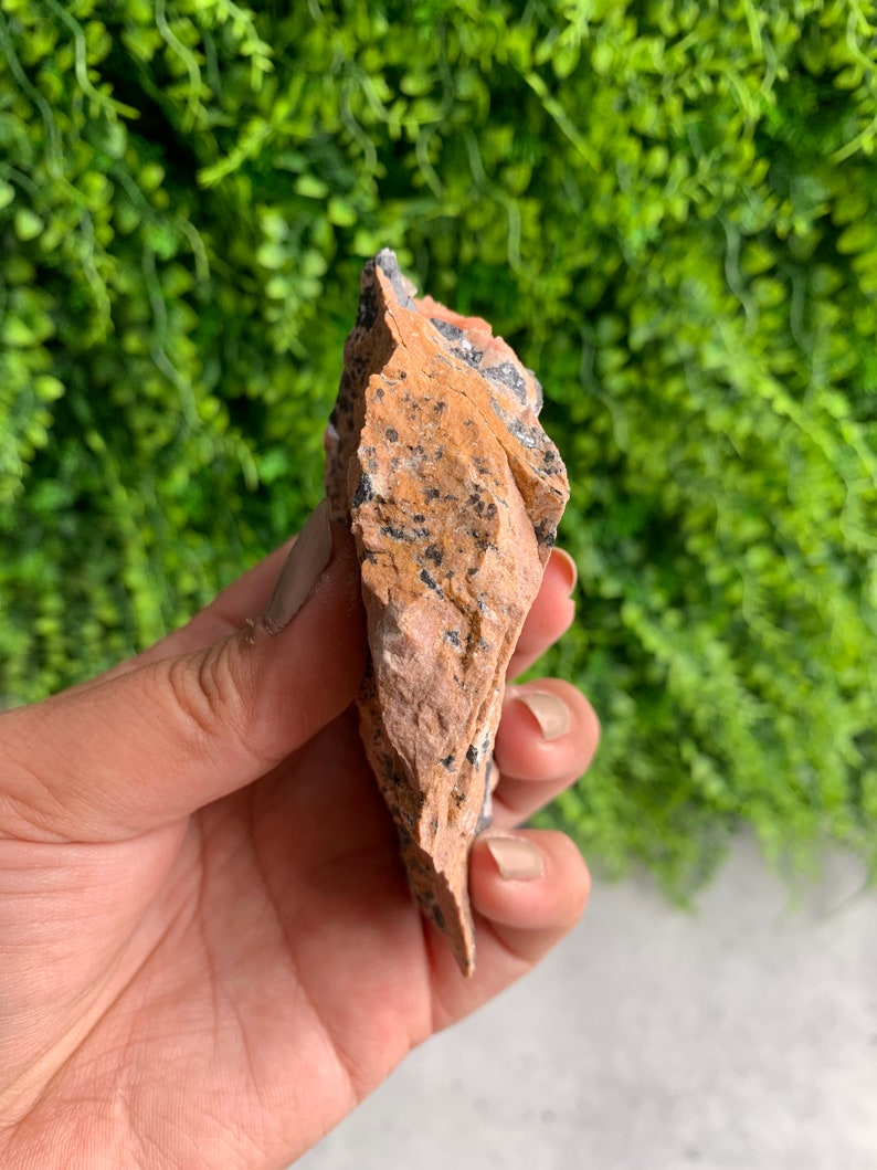 May include: A rough, orange-brown rock with black and white flecks. The rock is irregularly shaped and has a pointed tip.