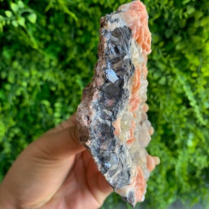 May include: A cluster of pink and white crystals with a dark gray metallic mineral. The crystals are arranged in a cluster and have a rough, natural texture.