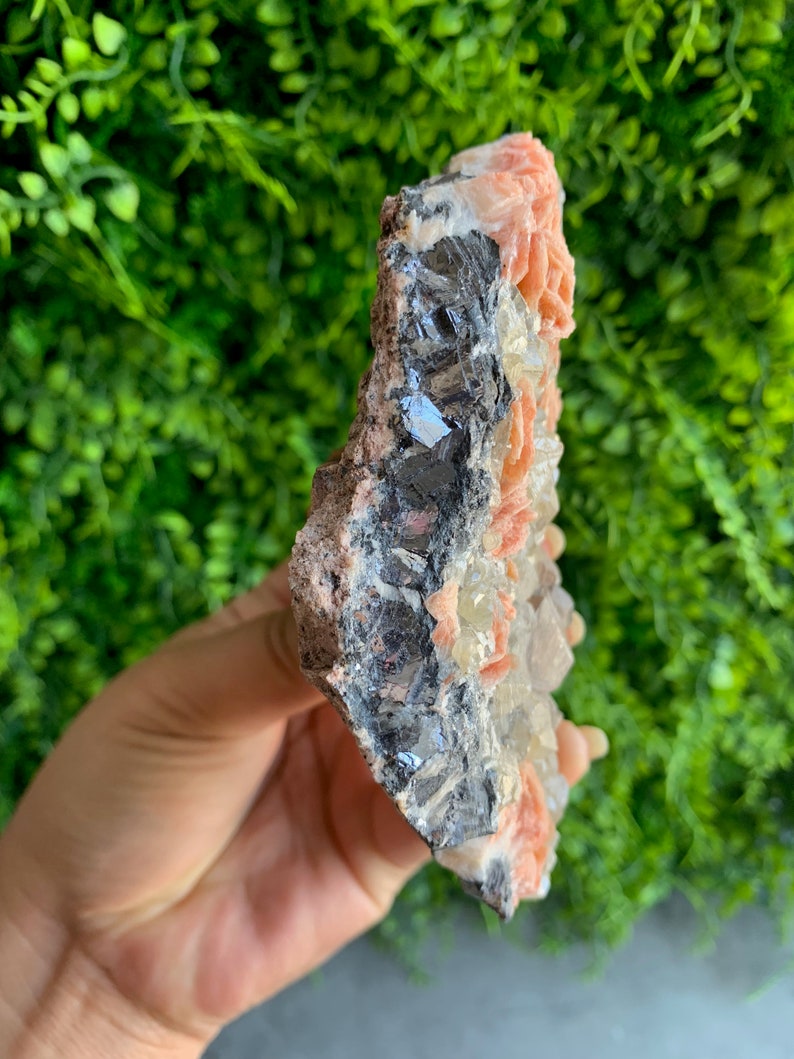 May include: A cluster of pink and white crystals with a dark gray metallic mineral. The crystals are arranged in a cluster and have a rough, natural texture.