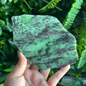 Pode incluir: Um cristal de zoisita verde, preto e rosa com uma textura áspera e natural. O cristal tem uma forma irregular e uma aparência manchada.