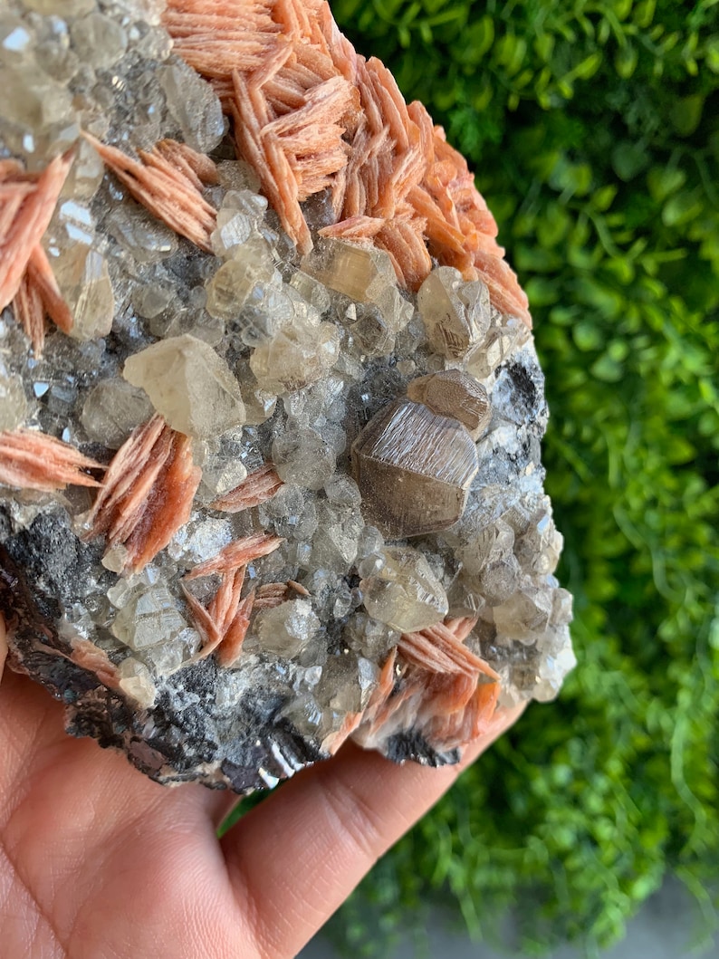 May include: A cluster of clear quartz crystals with a layer of orange-red barite crystals on top. The crystals are set in a dark gray matrix.