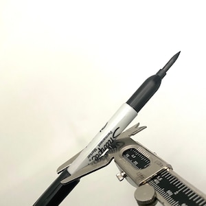 Puede incluir: Un marcador permanente negro Sharpie se está midiendo con una pinza de calibre plateado. La pinza de calibre indica 0,15 pulgadas.