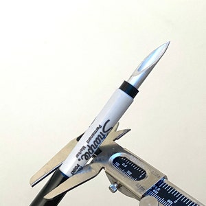 Puede incluir: Un rotulador permanente Sharpie blanco con texto negro y punta fina es sujetado por un calibrador plateado. La punta del rotulador es plateada. El calibrador mide el diámetro del rotulador.