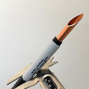 Puede incluir: Primer plano de una plumilla de caligrafía de cobre unida a un marcador permanente Sharpie. La plumilla se está midiendo con un calibre.