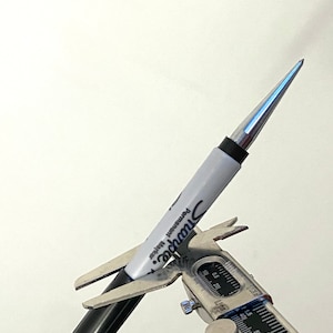 Puede incluir: Un marcador permanente Sharpie plateado con una punta fina se está midiendo con un calibre plateado. El calibre indica 0,5 mm.