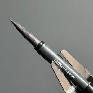 以下が含まれることがあります： 黒いOffice Depotのシャープペンシルのクローズアップ。鋭いグラファイトの先端が付いています。鉛筆は銀色の金属ボディと銀色の金属クリップが付いています。「Office DEPOT」の文字が鉛筆の側面に印刷されています。