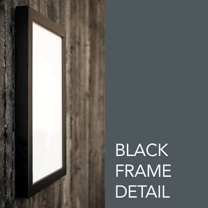 May include: A black picture frame with a white mat and a white background. The frame is hanging on a wooden wall.