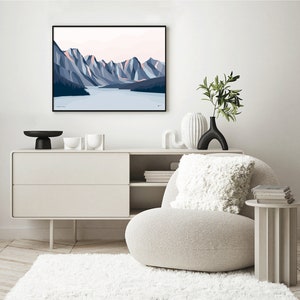 May include: A minimalist living room interior with a white armchair, a white side table, a white dresser with two drawers, and a framed print of a mountain landscape with a lake in the foreground. The print is in shades of blue and pink.
