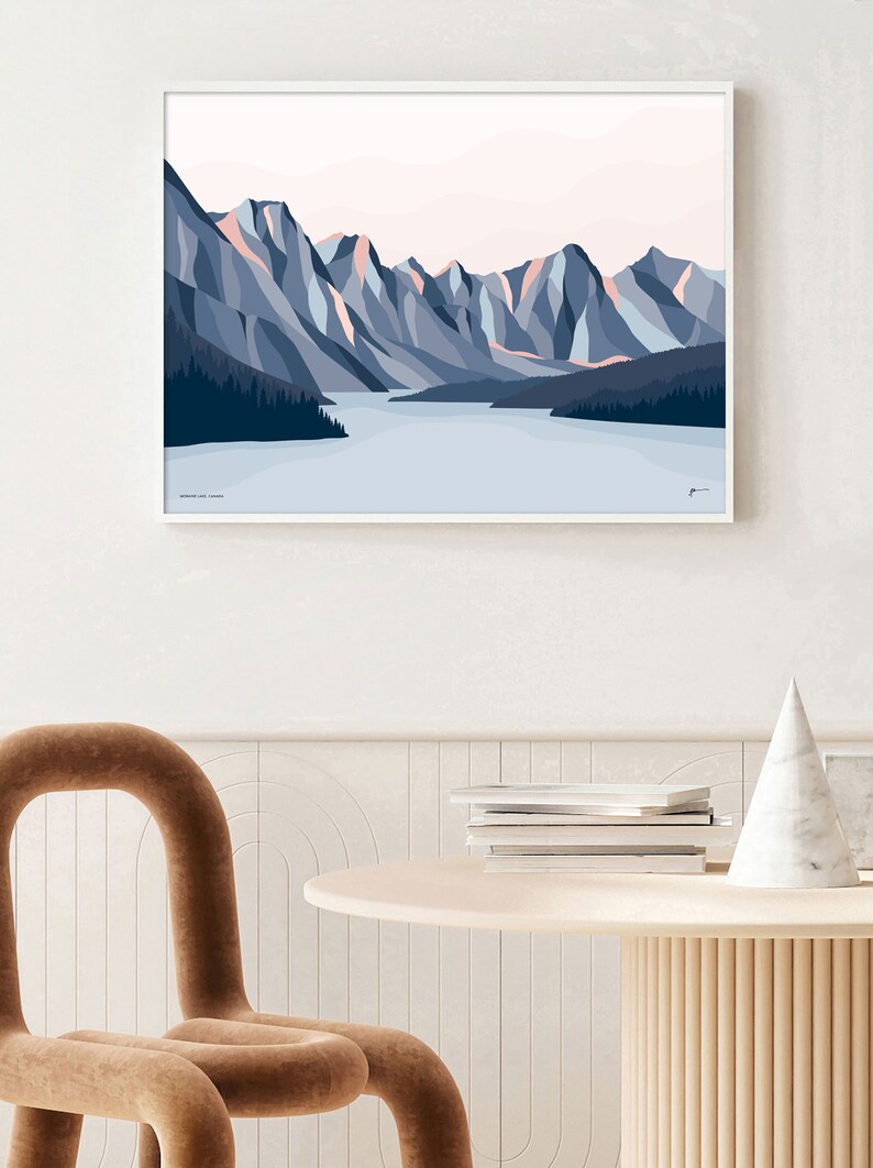 May include: A framed illustration of a mountain range with a lake in the foreground. The mountains are a mix of blue and pink hues, with a light blue sky above. The lake is a light blue color, and there are trees on the shore.