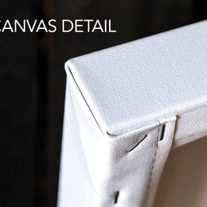 May include: Close-up of a white canvas print, showing the edge of the canvas and the staples holding it in place. The canvas is stretched tightly over a wooden frame.