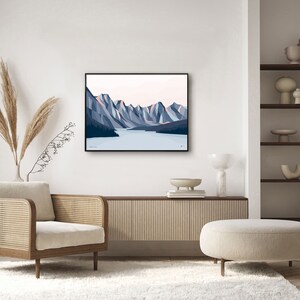 May include: A framed illustration of a mountain range with a lake in the foreground. The mountains are blue and pink, and the lake is blue. The illustration is in a black frame and is hanging on a white wall.