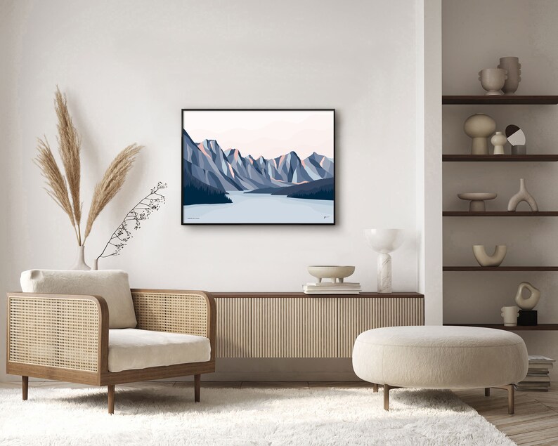 May include: A framed illustration of a mountain range with a lake in the foreground. The mountains are blue and pink, and the lake is blue. The illustration is in a black frame and is hanging on a white wall.