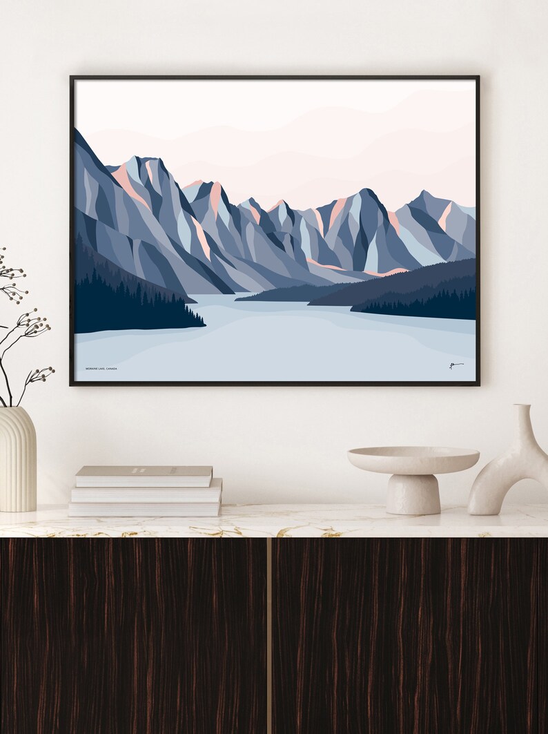 May include: A minimalist geometric illustration of a mountain range with a lake in the foreground. The mountains are shades of blue and pink, and the lake is a light blue. The text "Moraine Lake, Canada" is at the bottom of the image.