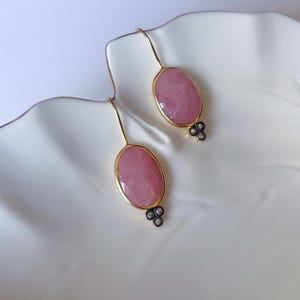 Pode incluir: Um par de brincos de ouro com pedras ovais cor-de-rosa e pequenos detalhes de diamantes.