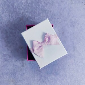 May include: A white gift box with a pink satin bow. The box is open and the inside is lined with pink paper.