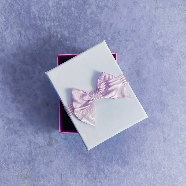 May include: A white gift box with a pink satin bow. The box is open and the inside is lined with pink paper.
