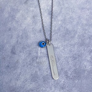 May include: Silver necklace with a blue evil eye charm and a silver pendant with Arabic calligraphy.