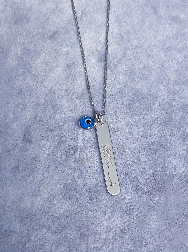 May include: Silver necklace with a blue evil eye charm and a silver pendant with Arabic calligraphy.