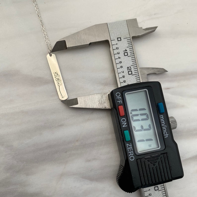 May include: A silver necklace with a small rectangular pendant that reads "Forever" in cursive. The pendant is being measured with a digital caliper, which reads 10.31 mm.